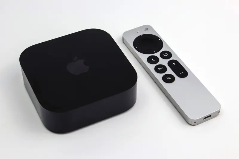 Apple TV 4K (3rd generation) set-top box beside its silver Siri Remote on a white surface